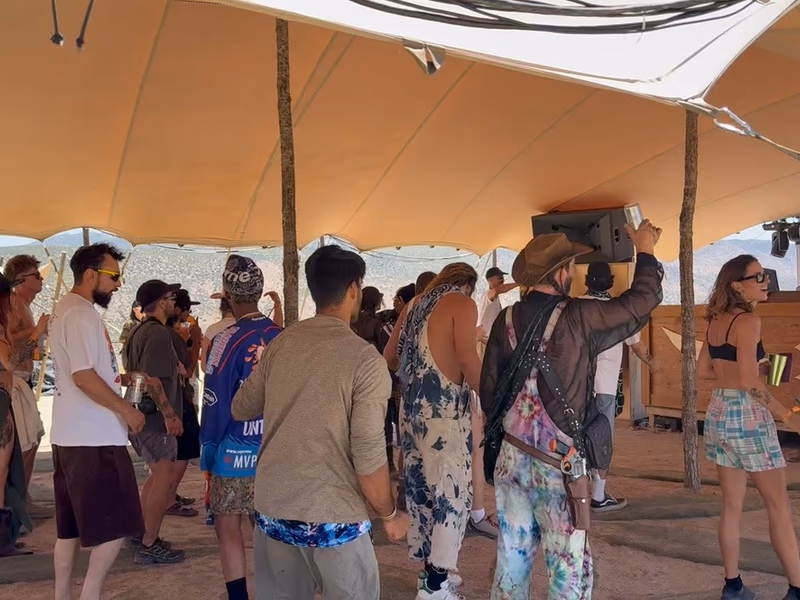 Festival guests dancing beneath a sand-colored stretch tent canopy