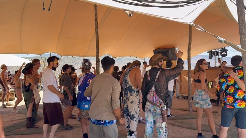 Festival guests dancing beneath a sand-colored stretch tent canopy