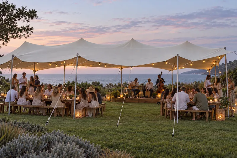 A coastal lawn party beneath a stretch tent with dinner tables and live musicians