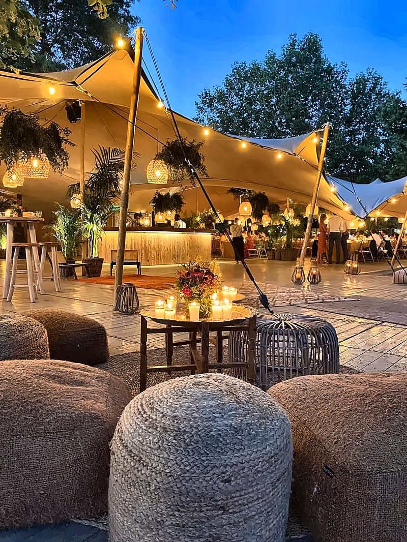 Stretch tent lounge with bar and woven poufs at dusk