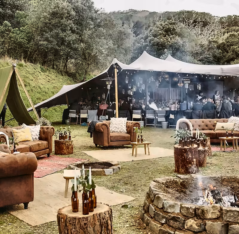Lounge with leather sofas and fire pit beside a dark stretch tent