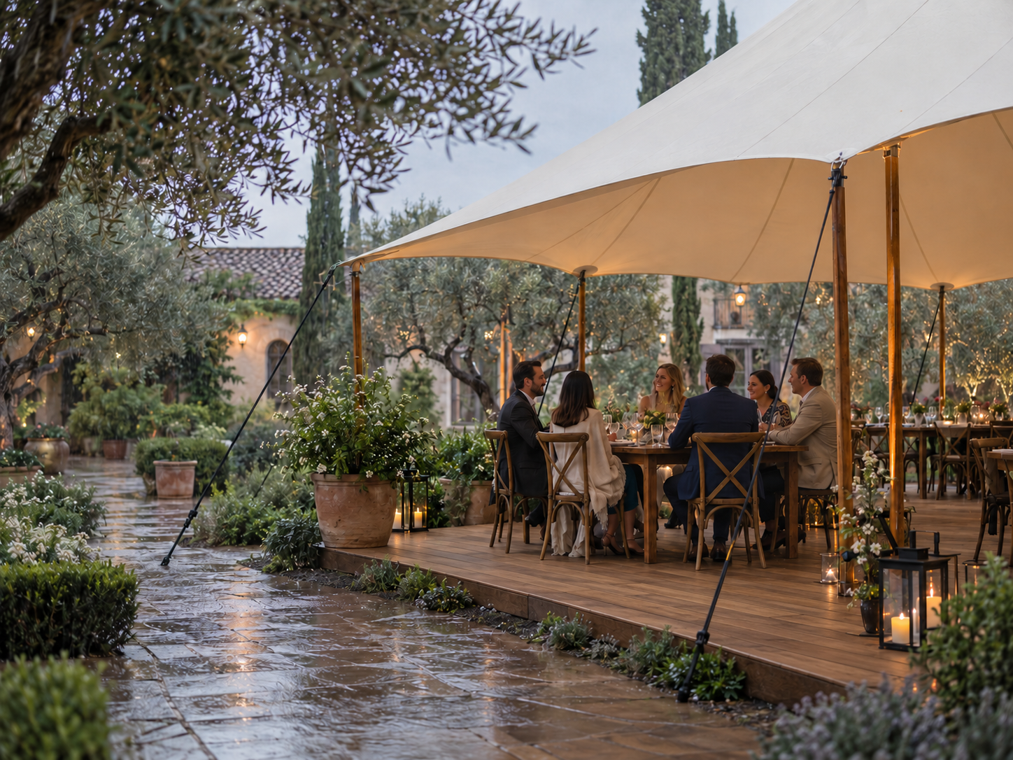 An outdoor reception under a stretch canopy with rain falling on the garden path outside